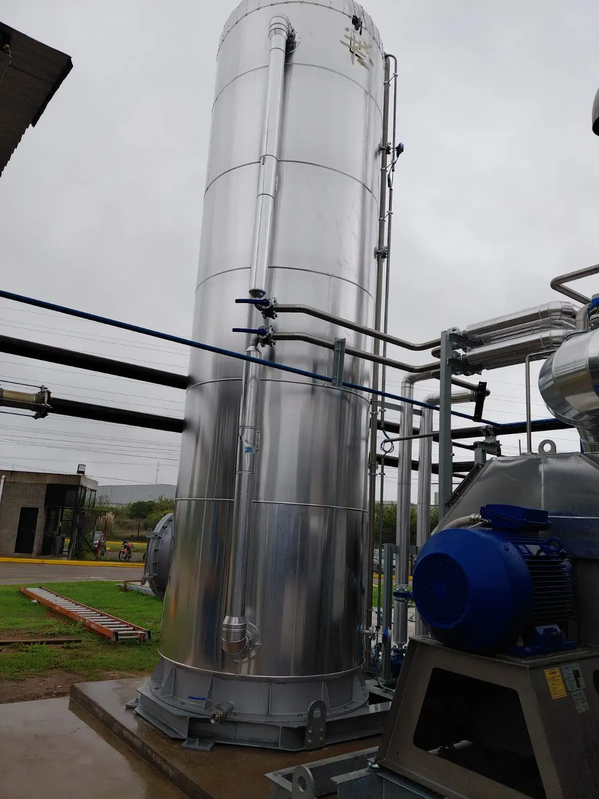 Jacketing completo en acero inoxidable sobre tanque vertical de gran altura con cañerías conexas y equipo en base, instalación exterior en planta industrial – Aislaciones DM