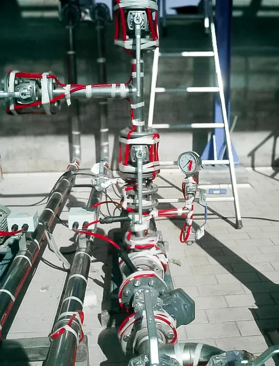 Tracing eléctrico con cables calefactores rojos instalados en manifold de cañerías con manómetros y válvulas en planta exterior – Aislaciones DM